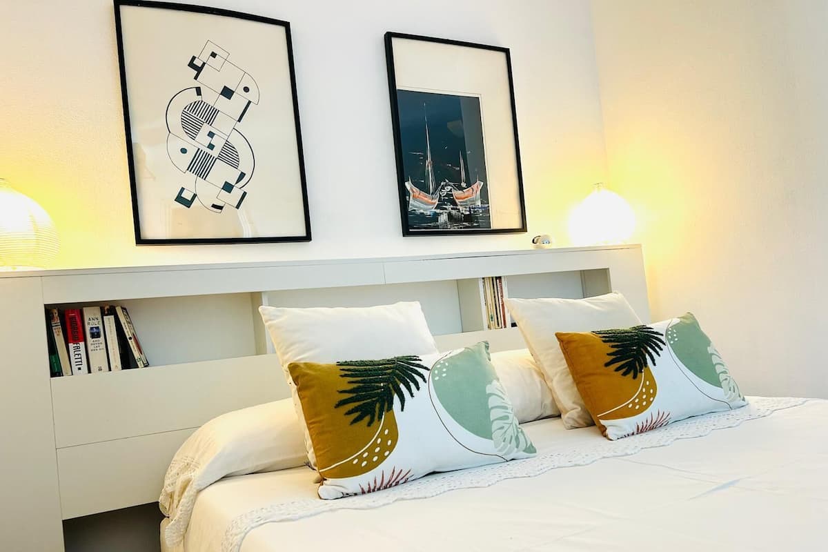 Un lit bien fait, avec deux oreillers, une tête de lit blanche et deux tableaux encadrés accrochés au mur.
