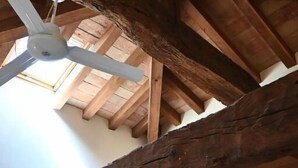 Una stanza con travi a vista in legno, una ventola a soffitto, una porta di legno e un televisore a parete.