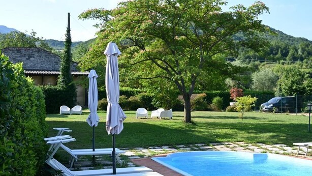 Una piscina con lettini e ombrelloni, immersa nel verde con una montagna sullo sfondo.