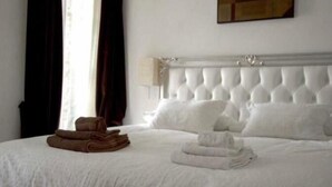 Un letto rifatto con asciugamani bianchi e marroni, una testiera capitonata e un quadro appeso al muro.