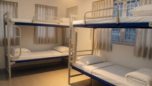 Una habitació amb tres llits superposats, cadascun amb una escala, i una finestra amb cortines.