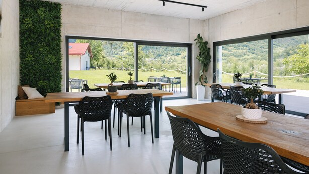 Un espace repas moderne avec une longue table en bois, des chaises noires en osier tressé et un mur vert.
