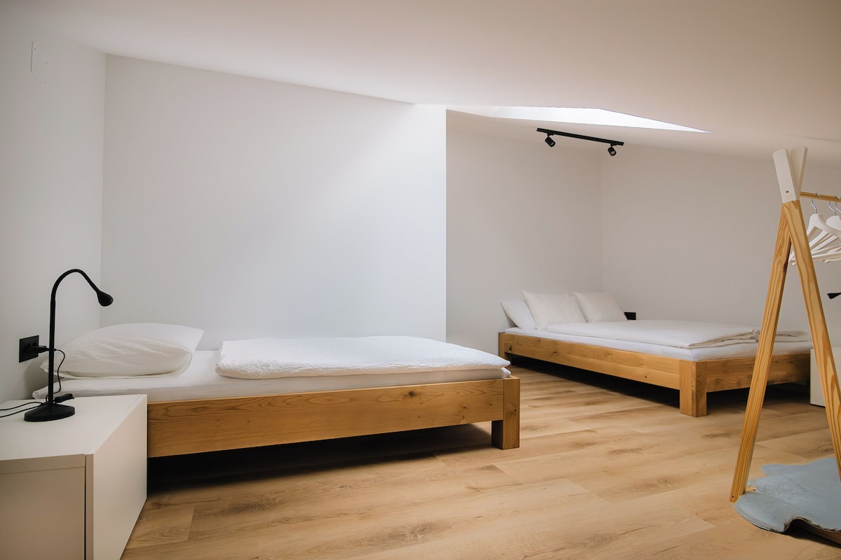 A minimalist bedroom with two wooden beds, a desk, and a hanging chair.