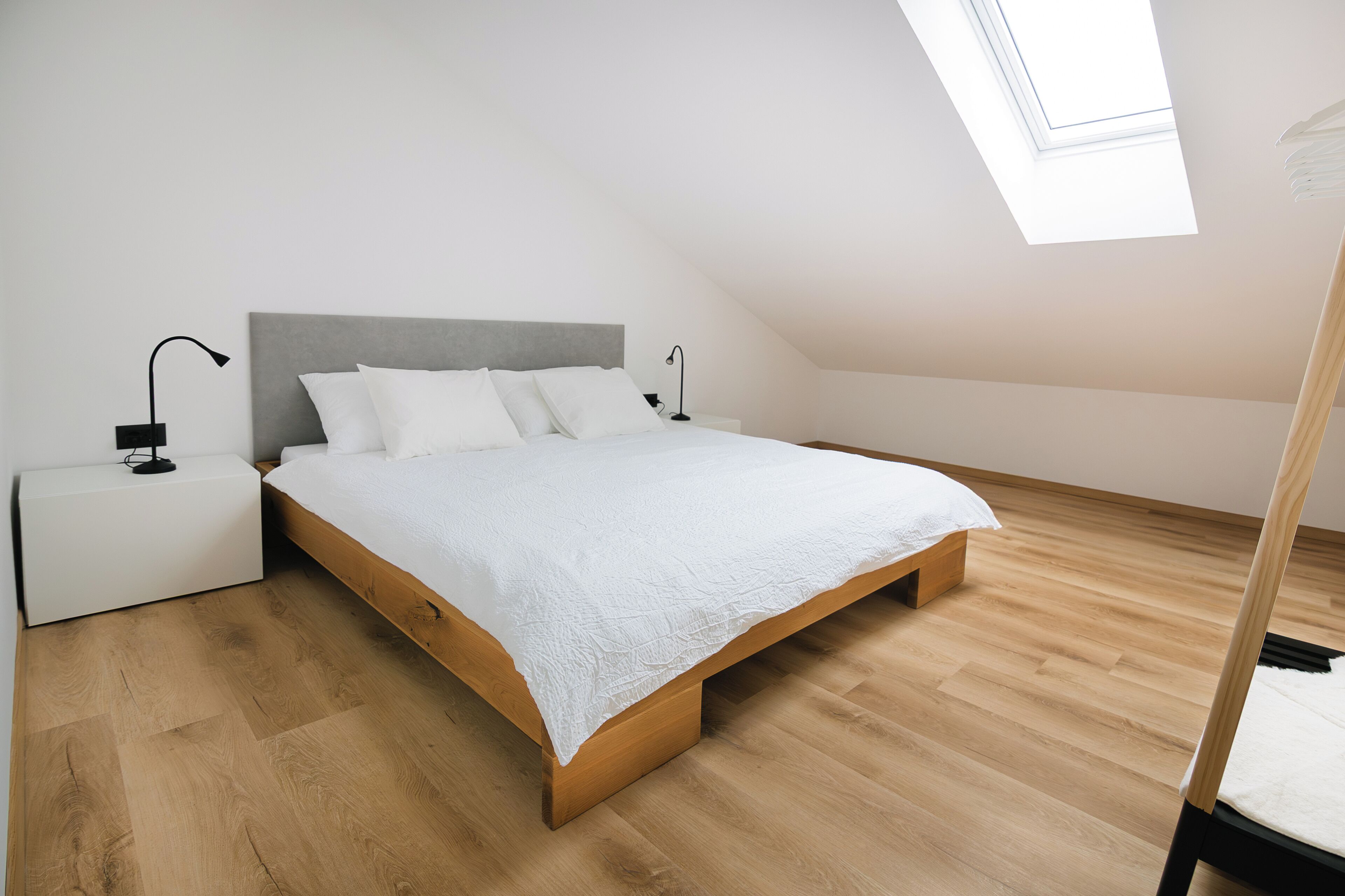 Un dormitorio con cama, mesitas de noche, tragaluz y suelo de madera.