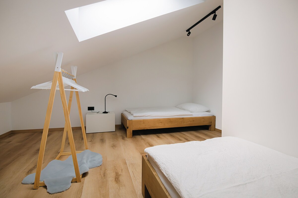 A bedroom with a skylight, wooden floor, a bed, a nightstand, and a hanging light fixture.