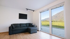 Un salon moderne avec un canapé d’angle, une œuvre d’art accrochée au mur et une grande porte-fenêtre coulissante donnant sur un paysage extérieur magnifique.