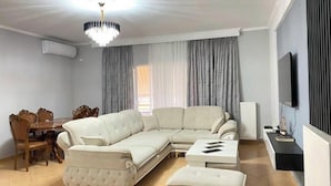 Una sala de estar con sofá modular, reposapiés, mesa de comedor con sillas y televisor.