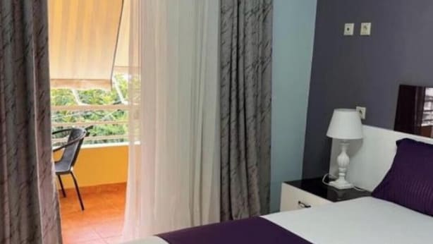 Habitación de hotel con cama, mesita de noche, lámpara y vistas al exterior.