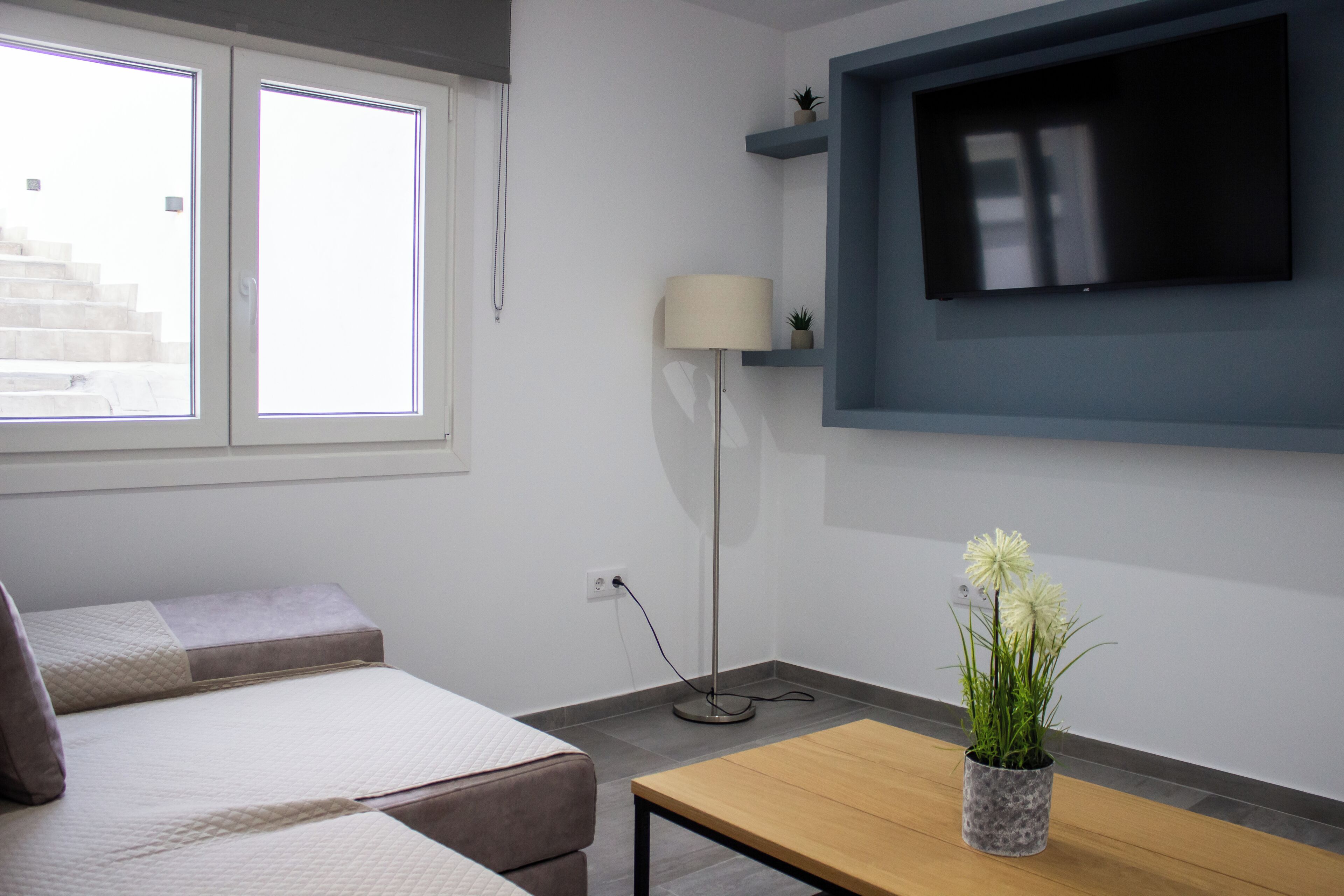 Une chambre moderne avec un lit, un téléviseur fixé au mur, une lampe et une petite plante posée sur une table.