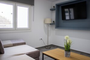 Een moderne kamer met een bed, een aan de muur bevestigde televisie, een lamp en een kleine plant op een tafeltje.