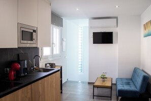 Een moderne keuken met een ingebouwde magnetron, een koffiezetapparaat en een spoelbak. Er is een blauwe bank en een kleine tafel met een plant.