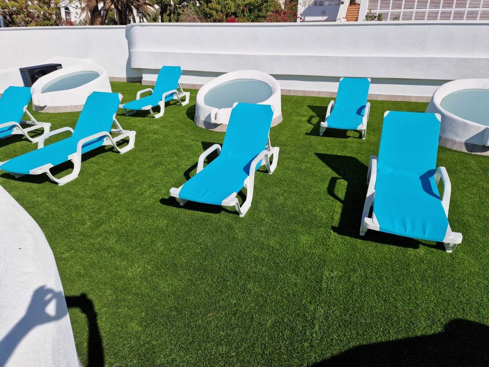 A rooftop pool area with artificial grass, white lounge chairs, and sun loungers.