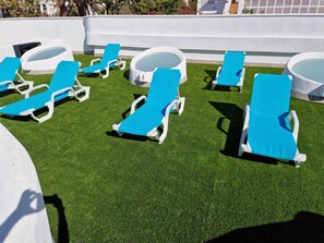 Een dakterras met zwembad, kunstgras, witte lounge stoelen en ligbedden.