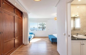 Ein Hotelzimmer mit Holzboden, einem großen Fenster mit Aussicht, einem blauen Sofa und einem Badezimmer mit Waschbecken und Spiegel.