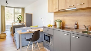 Een moderne keuken met grijze kastjes, een houten aanrechtblad, een inbouwoven en een raam met gordijnen.