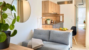 Een moderne keuken met houten kastjes, een ronde spiegel, en een zithoek met een grijze bank en een kleine tafel.