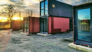 Una struttura moderna con facciata in vetro e rivestimento metallico, immersa in uno spazio aperto con terreno sterrato.