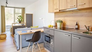Une cuisine moderne avec des meubles gris, un plan de travail en bois, un four encastré et une fenêtre avec des rideaux.