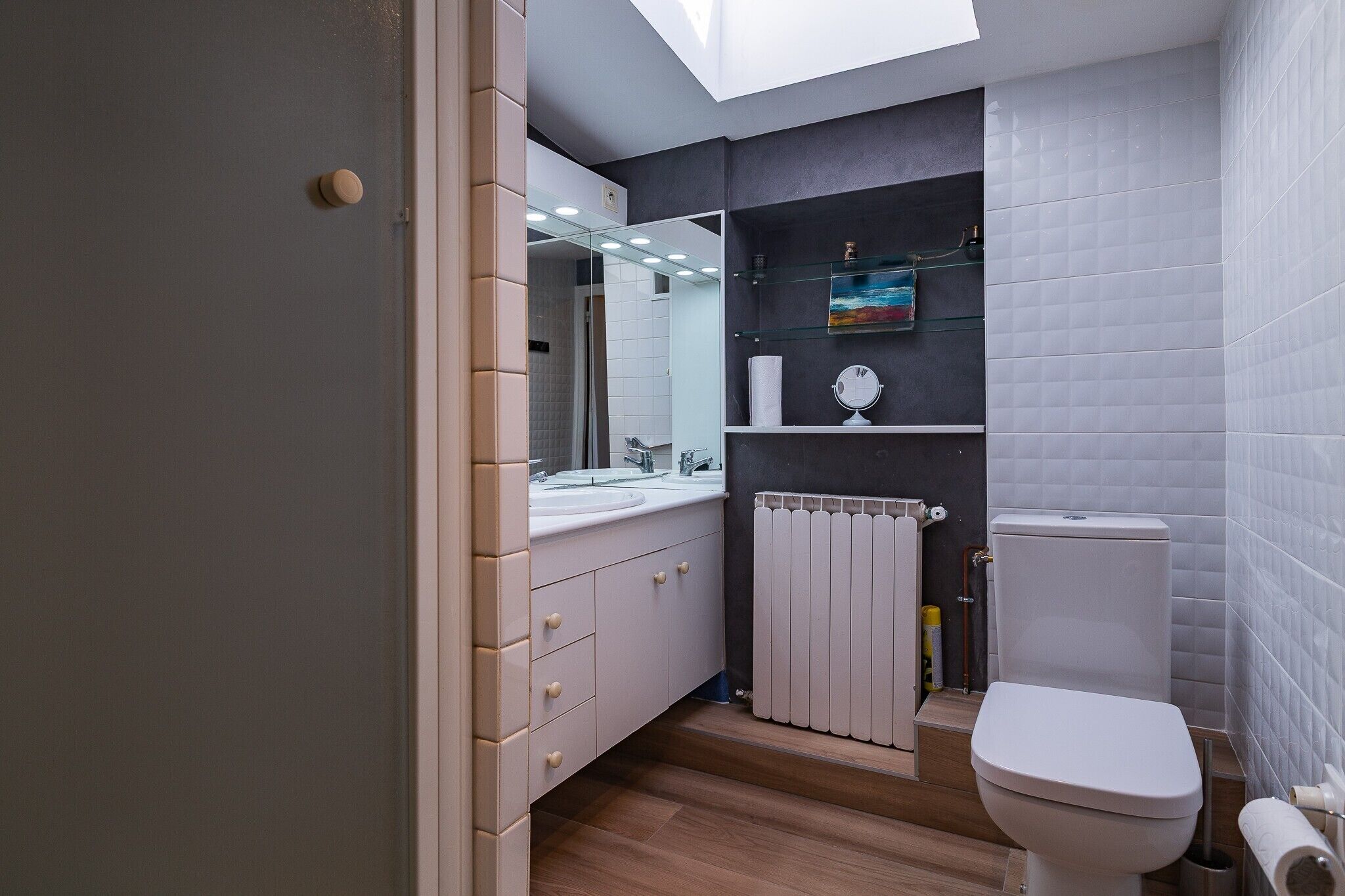 Un baño moderno con tragaluz, inodoro, lavamanos y espejo.