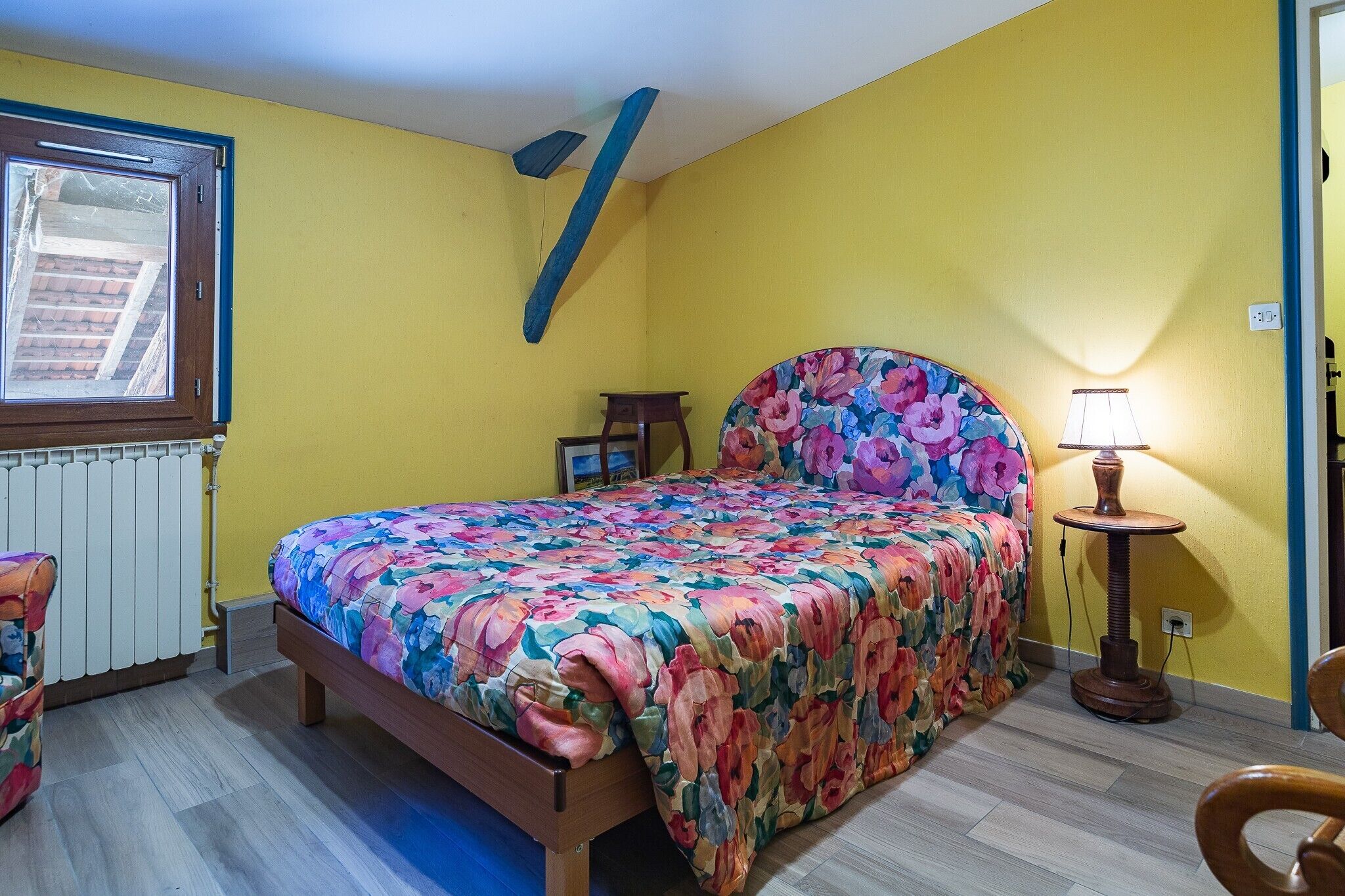 Un dormitorio con cama, mesita de noche, lámpara y ventana.