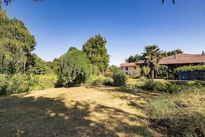A residential area with a grassy yard, trees, and a house with a red-tiled roof.
