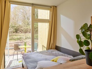 Un dormitori amb un llit, una finestra amb cortines, una planta en test i vista a l'exterior.