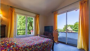 A hotel room with a bed, a television, a desk, and a balcony with curtains. - Gîte for 8 – La Fontaine Des Rollands: Mountain View, Shared Pool, Wi-Fi (Saint-Vérand)