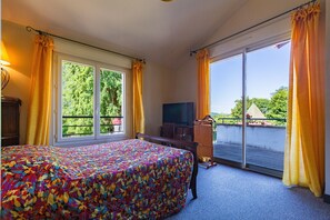 Une chambre d’hôtel équipée d’un lit, d’une télévision, d’un bureau et d’un balcon avec des rideaux.