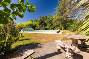 A swimming pool with a stone deck, surrounded by lush greenery and a clear blue sky.