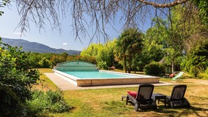 A rectangular swimming pool with a clear blue water surface, surrounded by a grassy lawn and various trees. There are two lounge chairs and a small table on the lawn. - Gîte for 8 – La Fontaine Des Rollands: Mountain View, Shared Pool, Wi-Fi (Saint-Vérand)