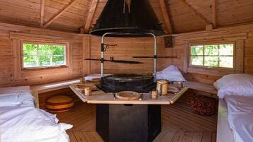 L’intérieur d’un chalet rustique est doté d’un poêle à bois central, de deux fenêtres et d’un lit avec un oreiller.
