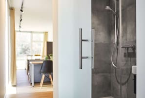 A modern bathroom with a shower, a glass door, and a visible kitchen area in the background. - Modern overseas container converted into a tiny house (Wertheim)