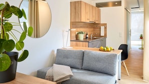 Una cocina moderna con armarios de madera, un espejo redondo y una zona de comedor con un sofá gris y una mesita.