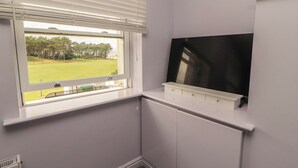 A corner room with a window, a flat-screen TV mounted on the wall, and a radiator below. - Sugar Loft (Wigton)