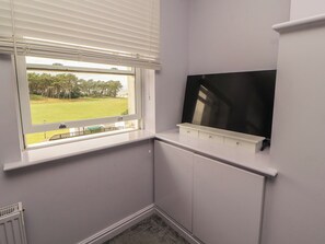 Habitació d'angle amb finestra, televisió de pantalla plana penjada a la paret i radiador a sota.