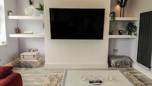 A living room with a flat-screen TV mounted on the wall, a coffee table with decorative items, and a red sofa. - Sugar Loft (Wigton)