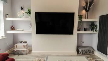 A living room with a flat-screen TV mounted on the wall, a coffee table with decorative items, and a red sofa.