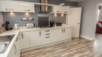 A modern kitchen with white cabinets, a stainless steel range hood, and a wood floor.