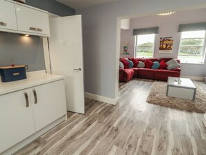 A modern living room with a red sofa, a white coffee table, and a kitchen area with white cabinets and a blue appliance.