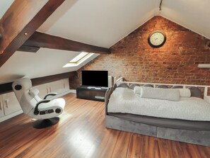 A loft bedroom with a sloped ceiling, exposed brick wall, a bed, a TV, and a massage chair.