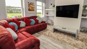 Een moderne woonkamer met een rode hoekbank, een flatscreen televisie en een lichtkleurige salontafel.
