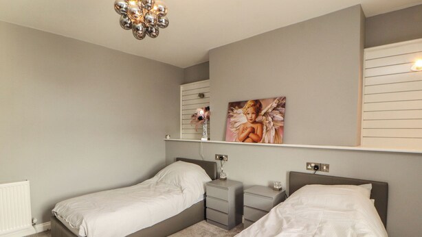 Een slaapkamer met twee bedden, een nachtkastje, een kapstok en een radiator, inclusief een plafondlamp.