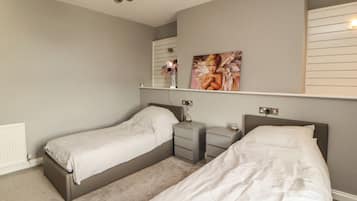 A bedroom with two beds, a nightstand, a dresser, a radiator, and a ceiling light fixture.