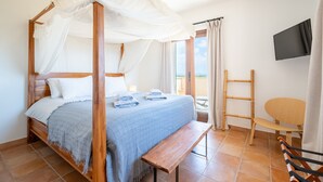 Ein Schlafzimmer mit einem Himmelbett, einer Bank, einem Fernseher und Balkonblick.