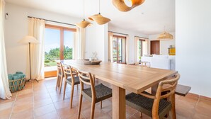 Ein geräumiger Essbereich mit einem Holztisch und Stühlen, großen Fenstern mit Vorhängen und hängenden Holzleuchten.