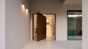 A modern hallway with a wooden door, a staircase, and a glass door leading outside. - Villa Neratzia-Luxury Escape (Neratzia)