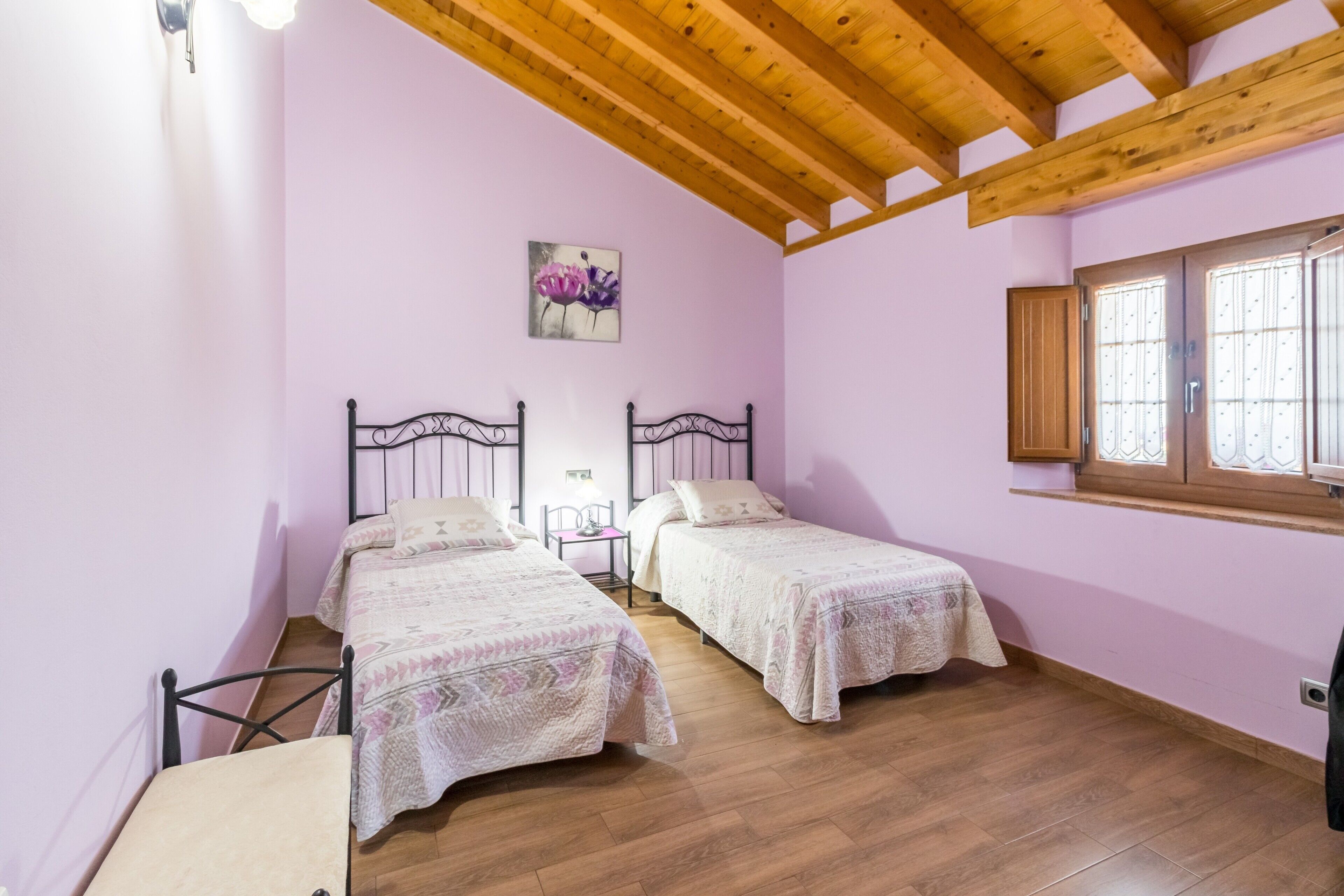 Una stanza con due letti, pavimento in legno, una finestra con persiane e soffitto in legno.