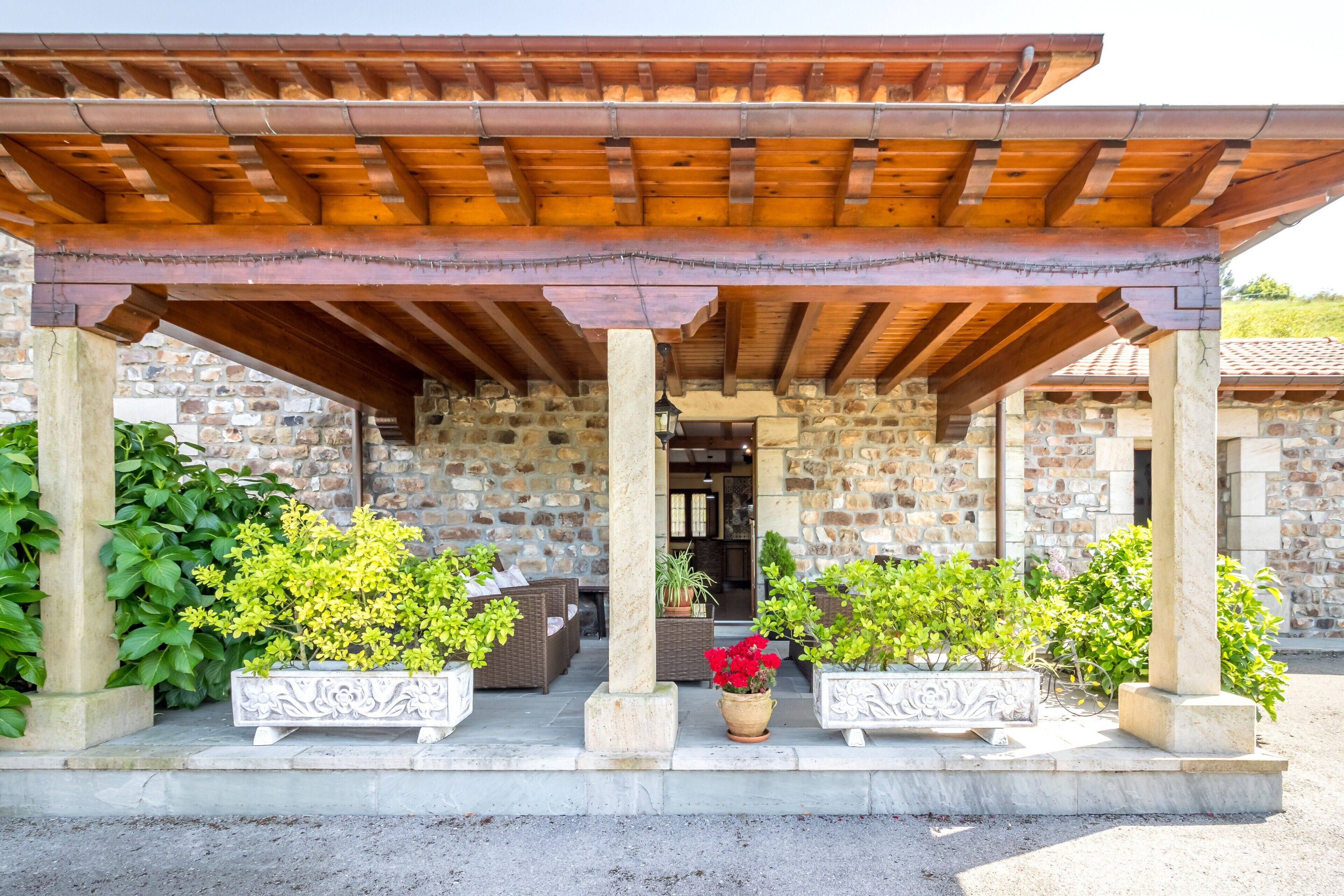 Un bâtiment en pierre agrémenté d’une pergola en bois, avec des espaces de repos en plein air et des plantes en pot.
