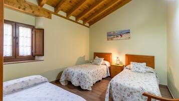 A bedroom with two beds, wooden beams, a window with blinds, a painting on the wall, and a nightstand with a lamp.