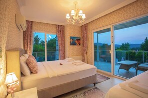 Quarto com cama grande, lustre, vista para o exterior e varanda com mobiliário.